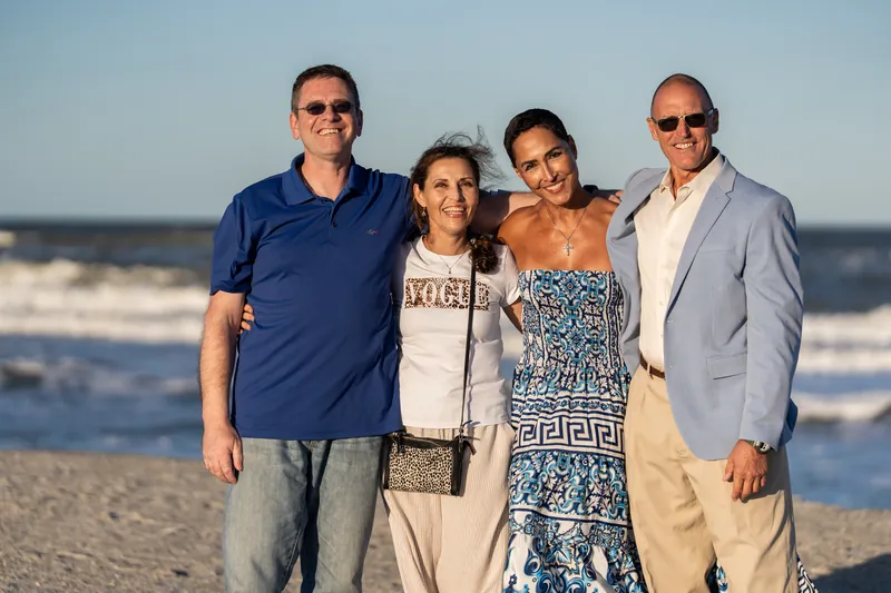 Four people stand shoulder-to-shoulder on the beach at St. Augustine, ocean waves visible under a clear blue sky.