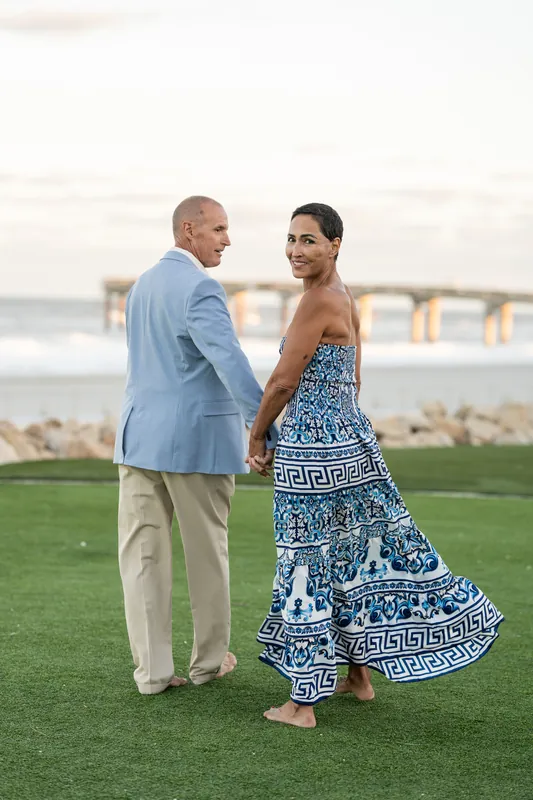 Jeff and Ella face each other on the lawn at St. Augustine Beach, the water and historic buildings visible behind them.