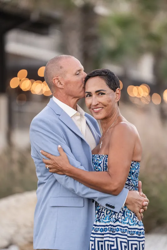 Two people embrace at sunset on St. Augustine Beach, with golden lights glowing behind weathered historic architecture.