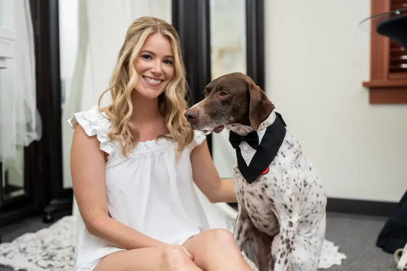 Jenna smiles warmly while posing with a brown and white dog wearing a black bow tie in the Lightner Museum Courtyard.