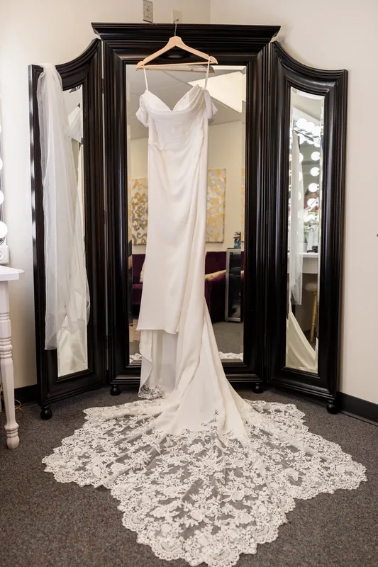 Jenna's white lace wedding gown hangs from an ornate black mirror in an interior dressing room.