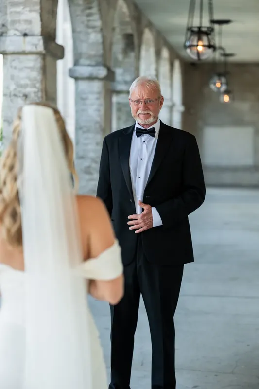 Russell stands in a black tuxedo with bow tie beneath the museum's arched colonnade, smiling warmly.