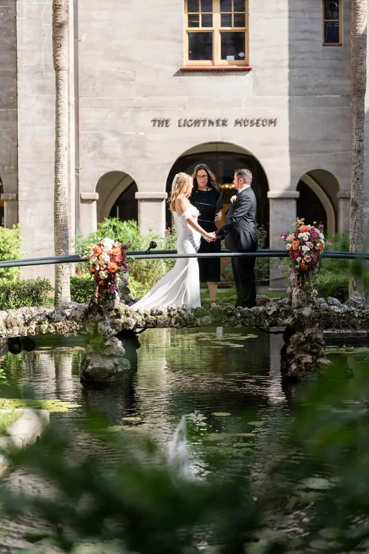 Jenna and Russell exchange vows on a stone bridge over the courtyard's reflecting pool at the Lightner Museum.