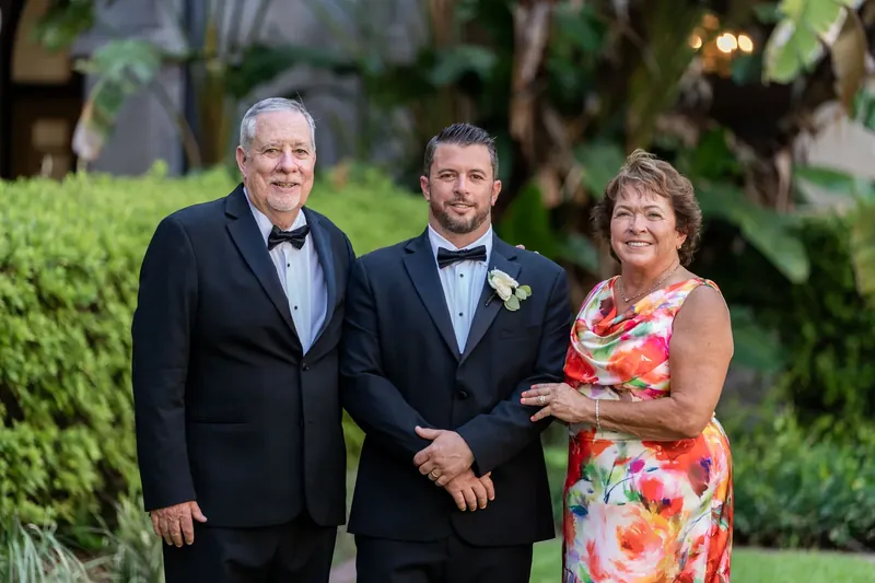 Russell poses with his father and mother on the courtyard grounds, all three smiling in formal attire.