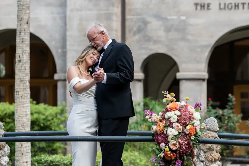 Russell and Jenna dance together on the courtyard terrace with a vibrant floral arrangement and historic architecture behind
