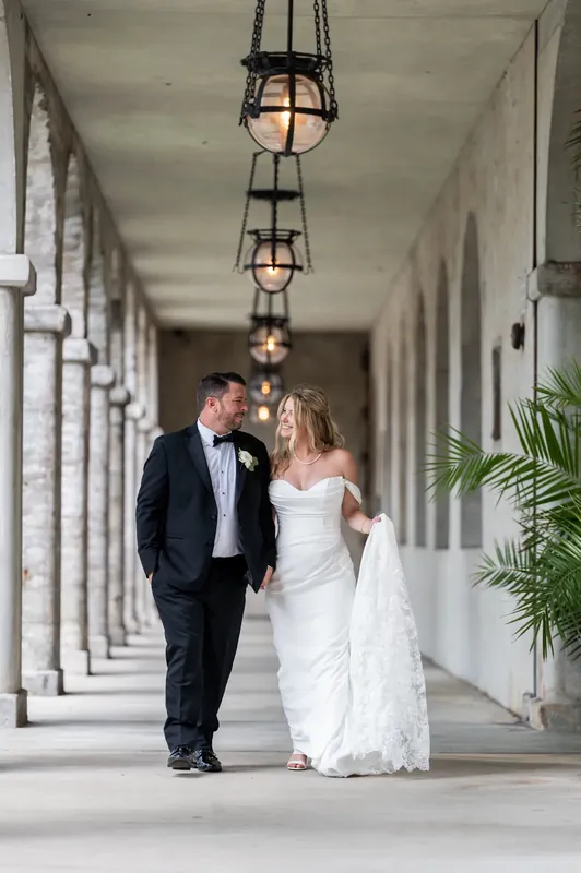 The couple stroll hand-in-hand down the columned walkway, Jenna's train trailing behind them as lanterns hang overhead