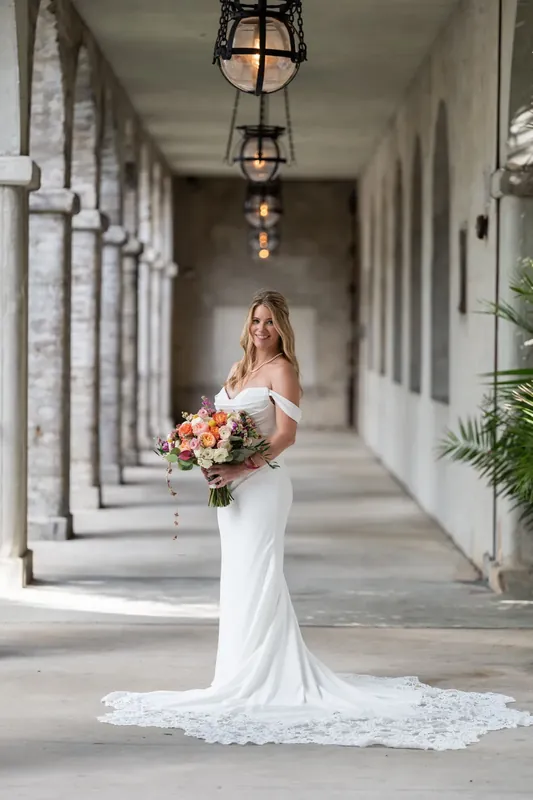 Jenna stands alone in her fitted white gown and cathedral train, holding her bouquet while centered in the symmetrical