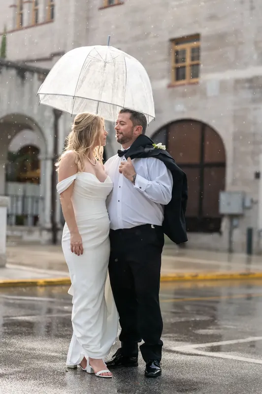 Jenna and Russell stand close under a clear umbrella on a rain-wet street in downtown St. Augustine.