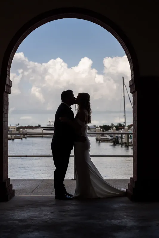 Silhouetted through a curved stone archway, the couple kiss with sailboats visible across the St. Augustine Bayfront behind