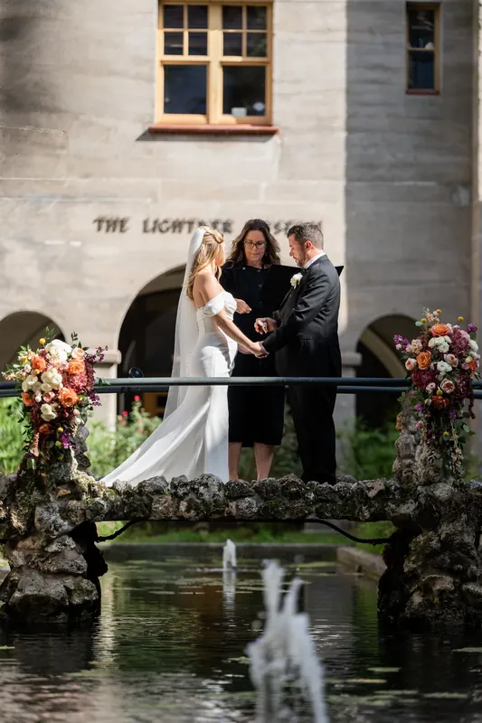 Russel kisses Jenna under a historic archway at the Lightner Museum as guests watch from behind iron railings.