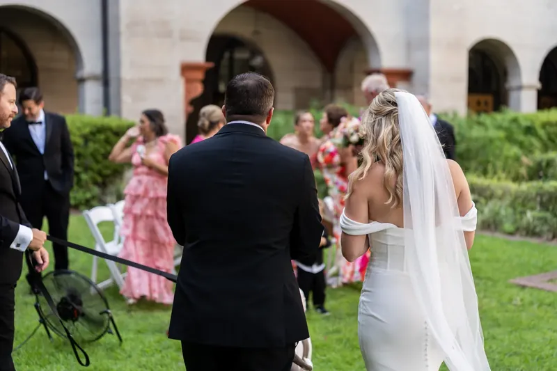 Jenna walks across the grass in her veil and gown while Russel turns to watch guests celebrating around them.