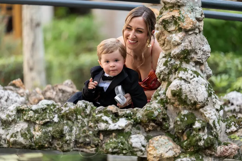 Jenna holds a toddler in a stone archway while both look toward the camera with bright smiles.