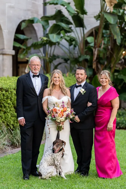 Four adults stand together on the lawn, with Jenna holding her bouquet and Russel in a tuxedo at the Lightner Museum.