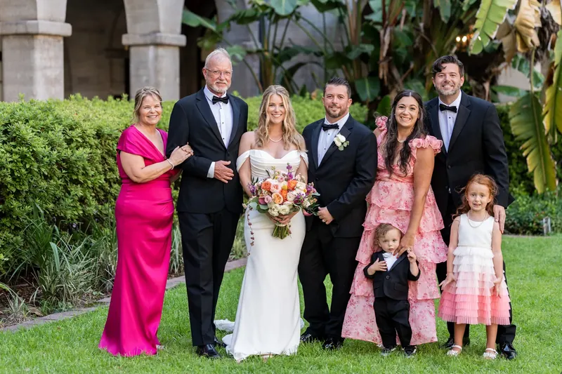 Multi-generational family group, including children in formal wear, gathers on the grass at the Lightner Museum Courtyard.