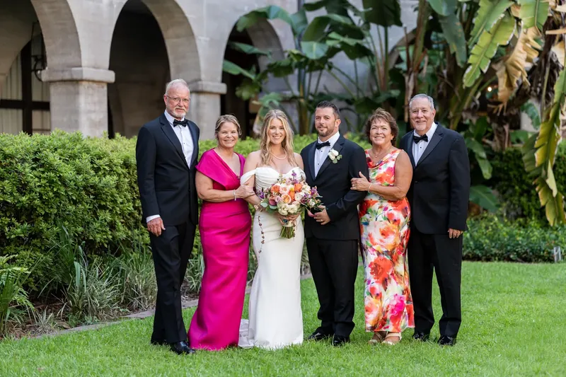 Six family members in formal wear pose on the courtyard lawn with stone arches framing them.