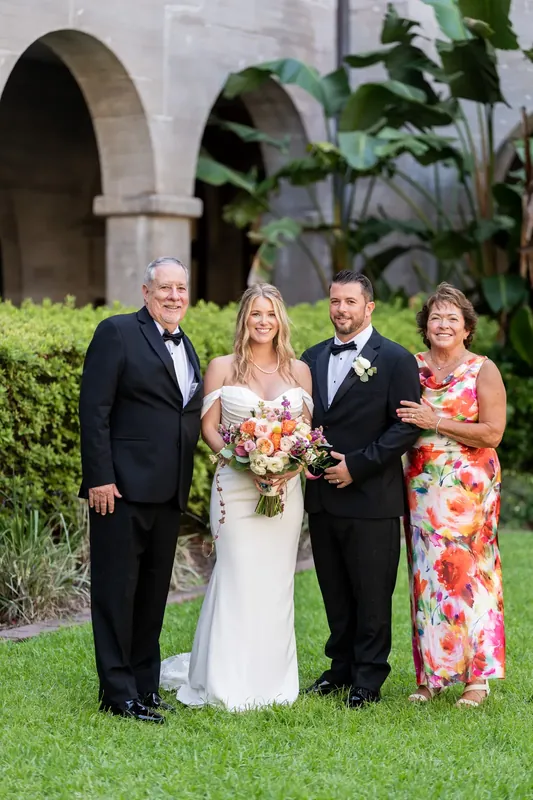 Russell, Jenna, and four relatives stand together on the grass beneath historic arched architecture.