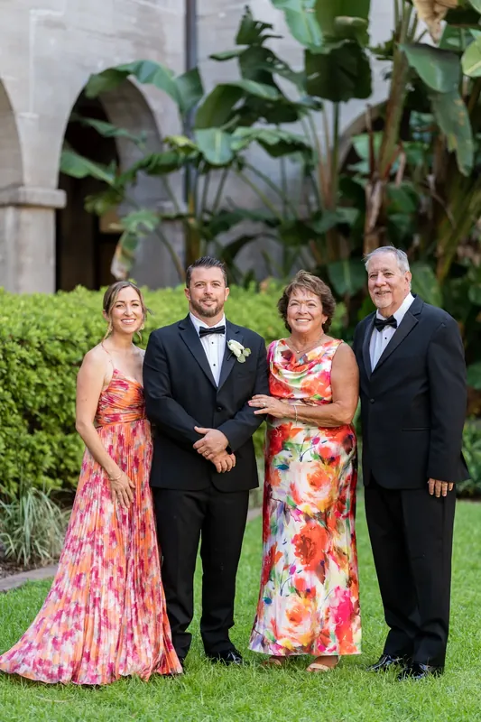 Russell stands between two parents and Jenna in a floral dress, all smiling on the manicured lawn.
