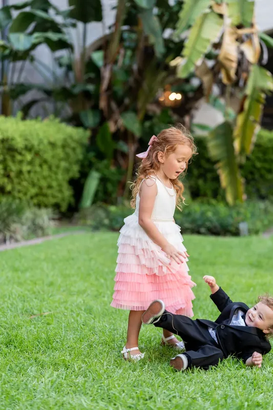 A young girl in a pink skirt plays with a child in formal wear on the grass.