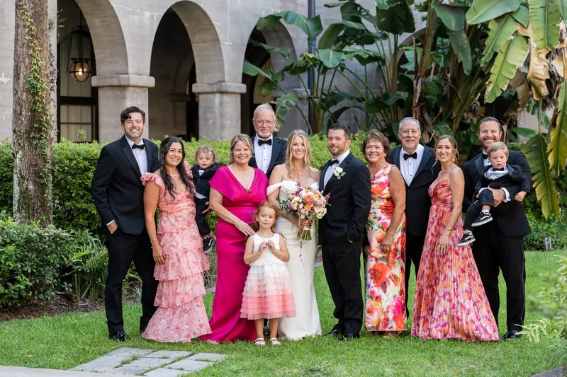 Eleven family members in coordinated pink and coral outfits pose together beneath arched architecture at Lightner Museum Courtyard.