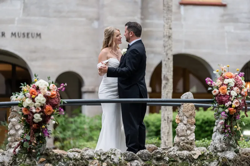 Russell and Jenna embrace on a stone bridge overlooking the courtyard's reflection pool, dressed formal.