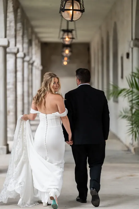 Russell and Jenna walk away through the arched passageway, her white gown's train sweeping behind them.