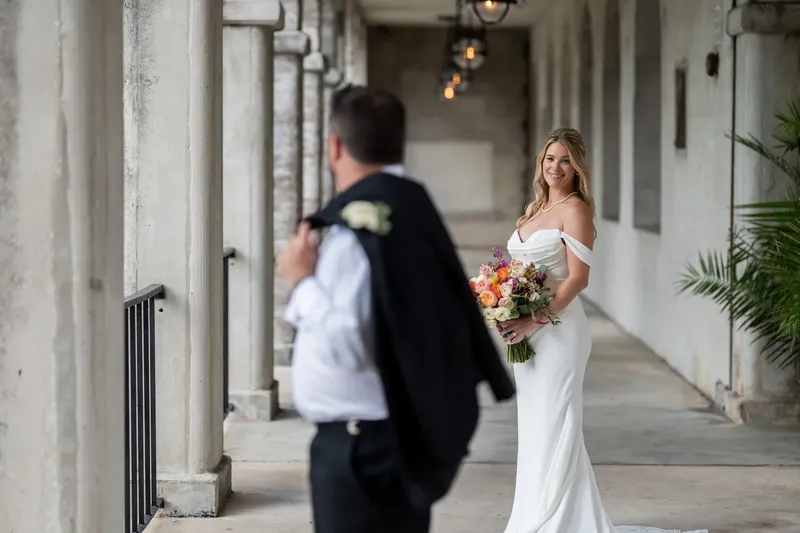 Jenna holds a blush and white bouquet while turning toward Russell in the Lightner Museum Courtyard colonnade.