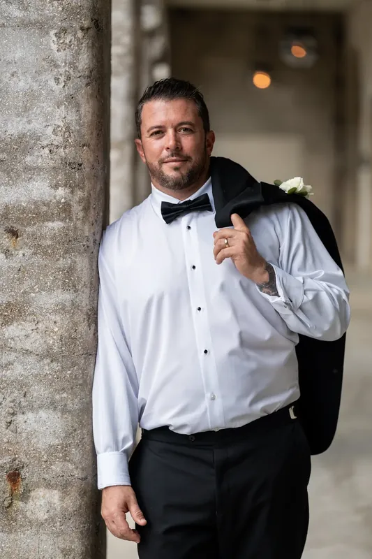 Russell leans against a stone column in a white dress shirt and black bow tie at the museum.
