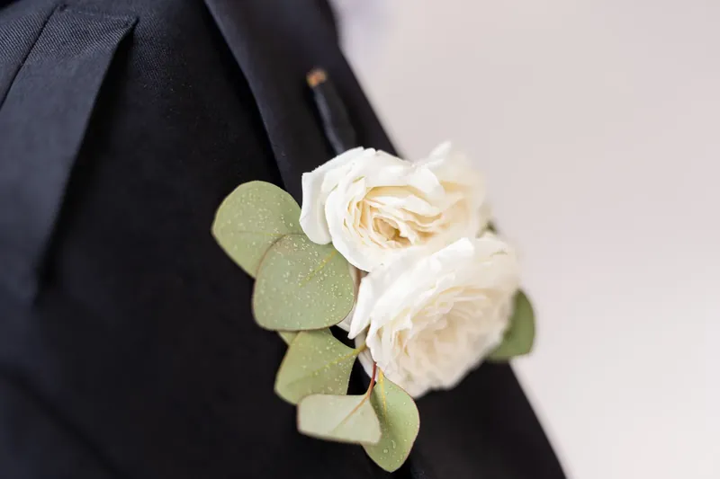 A white rose boutonniere with eucalyptus adorns Russell's dark jacket lapel.
