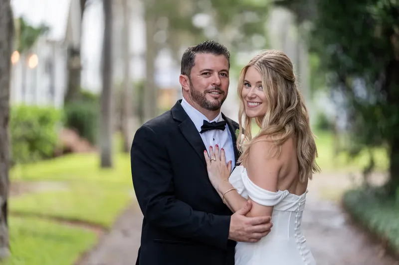 Jenna leans back against Russel as he wraps his arm around her waist on the shaded brick pathway.