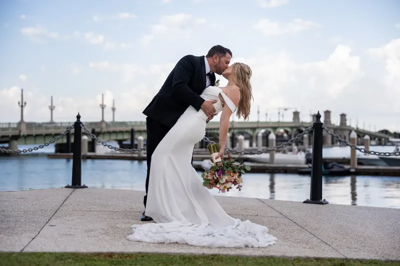 Russell dips Jenna as she holds her bouquet, her white gown's train flowing across the waterfront walkway.