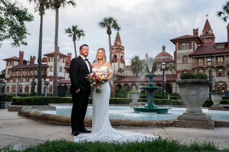 Jenna and Russell pose before castle-like architecture in Downtown St Augustine, she in white and he in a black tuxedo.