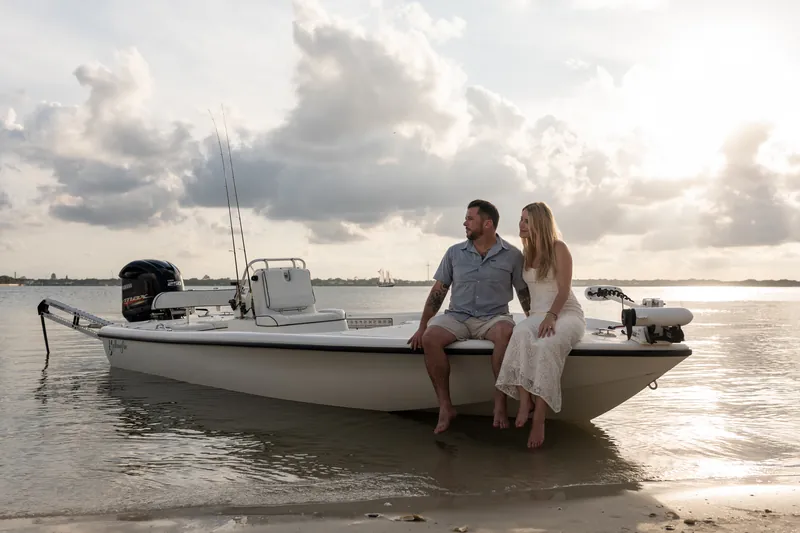 Russell and Jenna sit on the edge of their boat in the shallow water, leaning close together with golden light reflecting off