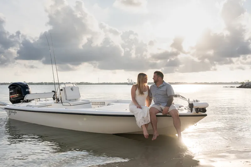 Jenna rests her head on Russell's shoulder as they sit on their boat's bow, the waterway and mangroves visible behind them.