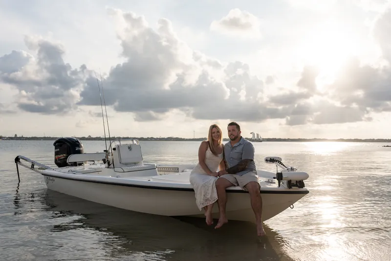 Russell wraps his arm around Jenna as they sit together on the boat, gazing out at the calm water under a bright, cloudy sky.