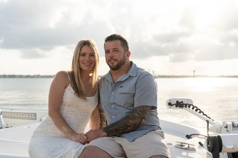Jenna and Russell sit close on a boat at Matanzas Inlet, holding hands while gazing at each other under cloudy skies.