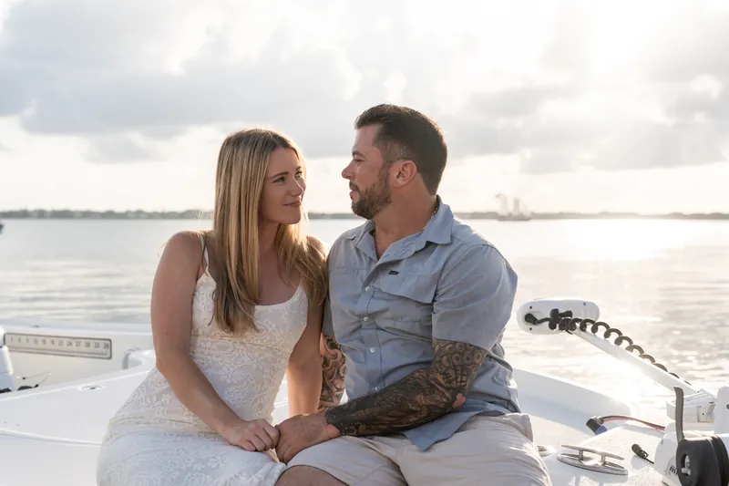 Russell and Jenna laugh together on the boat deck, with calm water stretching behind them.