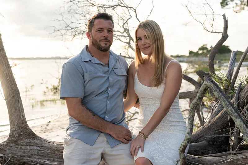 Jenna leans against a driftwood log while Russell sits beside her at Matanzas Inlet, both relaxed and content.