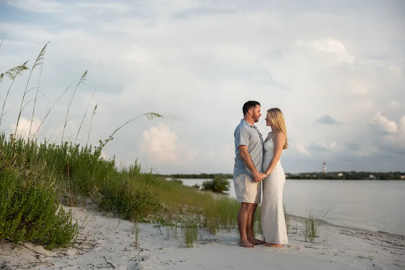 The pair stands on the beach among tall marsh grasses with calm water visible behind them.
