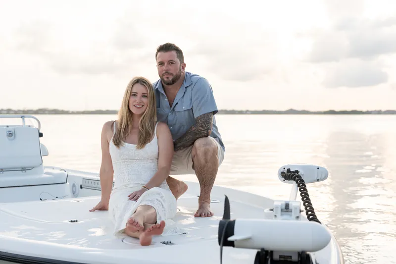 Seated on a boat at Matanzas Inlet, Jenna in white and Russell in blue lean close together with water and equipment visible