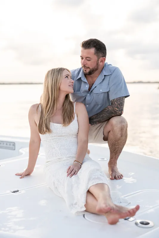 Russell crouches beside Jenna on the boat deck at Matanzas Inlet, both gazing at each other with calm water stretching behind