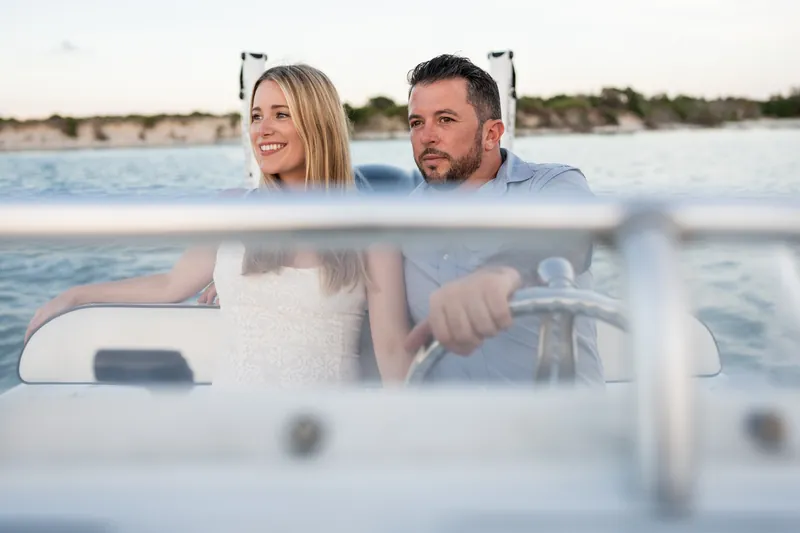 At the boat's wheel at Matanzas Inlet, Jenna and Russell sit side by side, both looking ahead with the shoreline visible