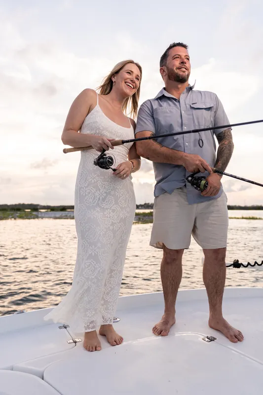 Jenna and Russell hold fishing rods side by side on a boat at Matanzas Inlet, both smiling in casual beach attire as water