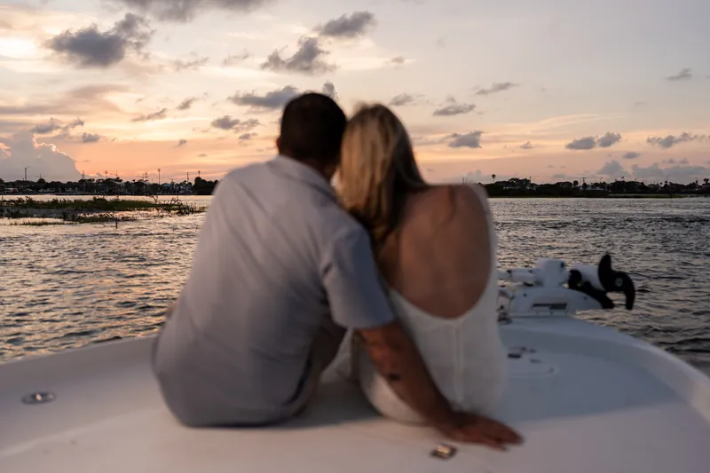 Seated on the boat's bow, Russell and Jenna face the sunset over the water, their silhouettes framed against the golden sky.