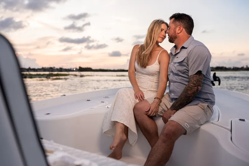 Jenna tilts her head toward Russell's shoulder while sitting on the boat, both laughing as the sunset glows across the inlet