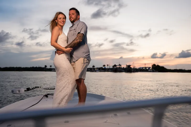 Russell lifts Jenna in his arms while standing in the shallow water at Matanzas Inlet at sunset, both smiling as the sky
