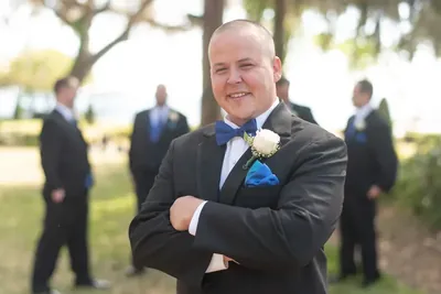 Groom in black suit with blue bow tie smiling outdoors with groomsmen