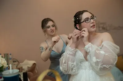 Bride putting on earrings with bridesmaid helping