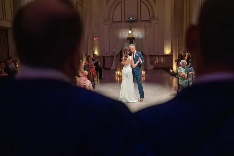 A newlywed couple shares their first dance as husband and wife surrounded by family and friends in a beautifully lit hall