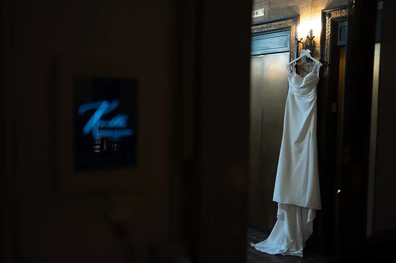 A white wedding dress hangs on a doorway with trailing fabric visible in the foreground at The Treasury on the Plaza.