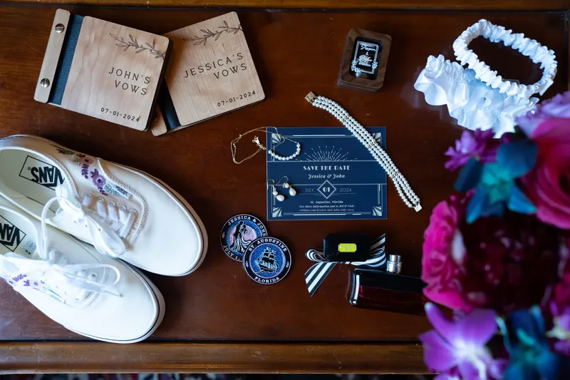 White sneakers, wedding programs, blue stationery, and colorful flowers arranged on a wooden table for getting-ready details.